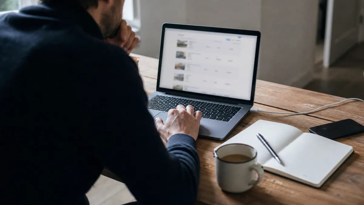 Persoon vergelijkt op een laptop meerdere aanbiedingen van domeinnamen aan een bureau met notitieblok
